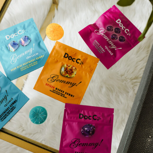 DocC. Gemmy! cannabis gummies assortment featuring Sour Blue Raspberry Deuce, Spiced Mango, Grape Gummy, and Quad Grape formats displayed in a lifestyle flat-lay setting.